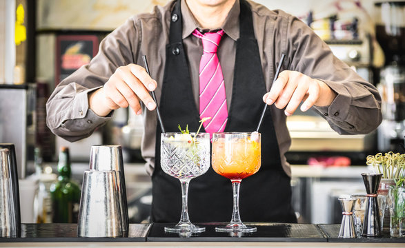 Classic bartender serving gin tonic and tequila sunrise with straw on drink glasses cups at fashion cocktail bar - Food and beverage concept with professional barman working at mixology restaurant