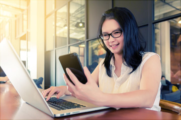 Asian charming beautiful girl freelancer in casual suit working or check information from website on her laptop and smartphone or mobile phone in coffee shop or modern office. Business Concept.