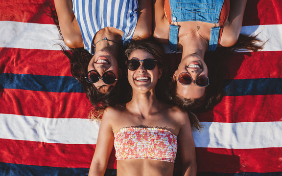 Three girl friends lying on striped towel on the beach