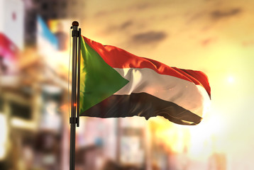 Sudan Flag Against City Blurred Background At Sunrise Backlight - obrazy, fototapety, plakaty