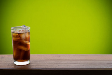 cola with ice in glass on wooden board with green  background  for refreshment; eagerly; refreshing, conceptual