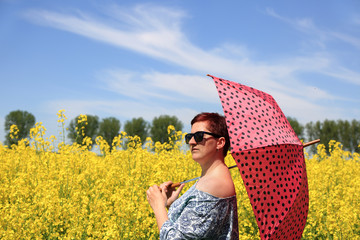Kobieta z parasolem na tle kwitnącego rzepaku. - obrazy, fototapety, plakaty