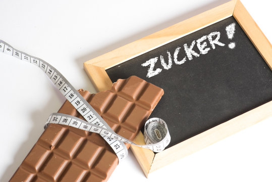 Eine Tafel Schokolade, Massband und eine Kreidetafel mit dem Wort Zucker