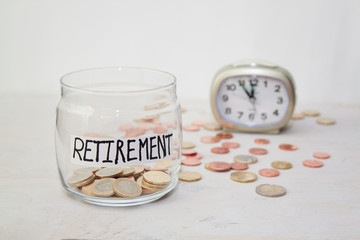 Close up Coins in glass jar with alarm clock for time to money saving for retirement concept , vintage color tone