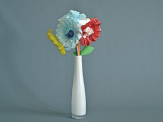 fiori di plastica riciclata, dentro un vaso tubolare bianco, con colori e sfindo di diverse...