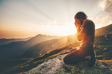 Man praying at sunset mountains Travel Lifestyle spiritual relaxation emotional meditating concept vacations outdoor harmony with nature landscape - obrazy, fototapety, plakaty