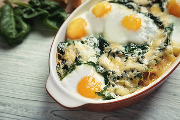 Baking dish with delicious cooked eggs Florentine on wooden background