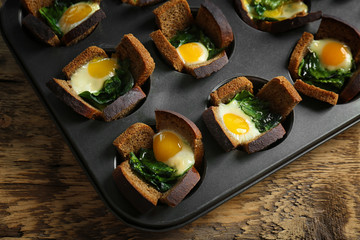 Baking mold with eggs and spinach on wooden table