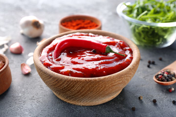 Wooden bowl with tasty chili sauce on grey textured table