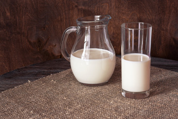 Milk in a glass and a glass jug on a wooden table