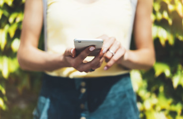 Hipster text message on smart phone or technology, mock up of blank screen. Young girl using cellphone on yellow flower background close. Tourist female hands holding gadget on blurred summer backdrop