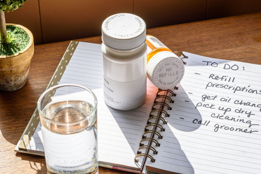 Pill bottles on nightstand with handwritten to-do list and glass of water