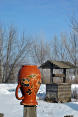 Traditional Ukrainian rural landscape with a wooden well and fence with hanging pitcher on it with Petrykivka folk painting, snowy winter day