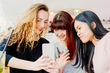 Three young girlfriends playing with ipad, reviewing holyday photos