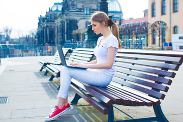 A girl is sitting on a bench and working on a laptop in a European city dresden