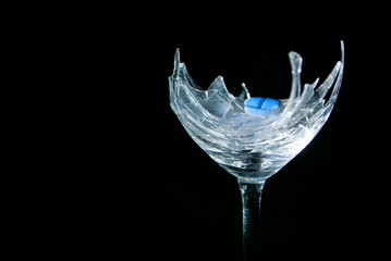 Blue pill on broken wineglass on black background