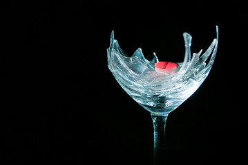 Red pill on broken wineglass on black background
