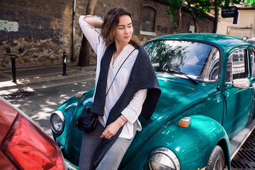 Beautiful woman standing near car. Young pretty hipster cheerful girl posing on the street at sunny day