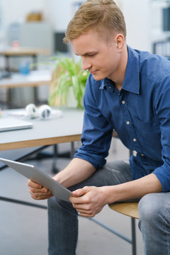 junger mann sitzt am schreibtisch und schaut auf tablet