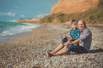 Weekend at the beach Dad and son sitting on the beach and looking at each other. A beach Stone sea...