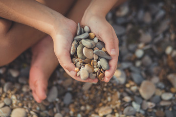 Woman hands holding small stones in hands on beach background with burning sun