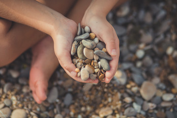 Woman hands holding small stones in hands on beach background with burning sun