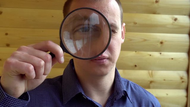 The big face of a curious man looking at the camera with a magnifying lens (a detective private eye).