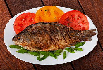 Roasted river fish carp on a white plate with tomatoes
