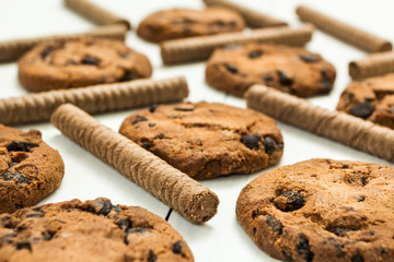 Chocolate wafer rolls and freshly baked chocolate homemade cookies on a white wooden table.