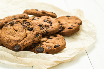 Freshly baked chocolate homemade cookies on parchment paper with a white wooden table.