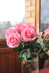 Bouquet of pink lush roses in a vase at an open window on a street background