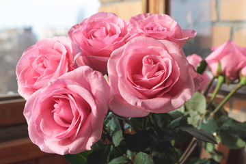 Bouquet of pink lush roses in a vase at an open window on a street background