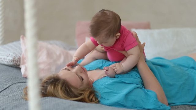 Joyful mother playing with her baby infant in bed