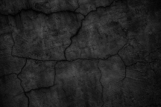 Black concrete wall covered with cracks. Gloomy surface of the cement board