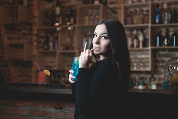 Beautiful attractive brunette young woman drinking blue lagoon cocktail in night club. 