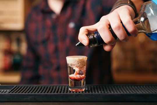 Handsome bearded barman is making monkey brain cocktail in night club. 