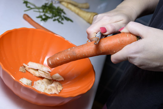 woman hands peeling a carrot on a wooden board