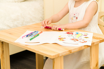 Obraz na płótnie Canvas Active little preschool age child, cute toddler girl with blonde curly hair, drawing picture on paper using colorful pencils and felt-tip pens, sitting at wooden table indoors at home or kindergarten