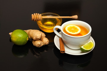 Cup with tea, raw ginger and lime on saucer