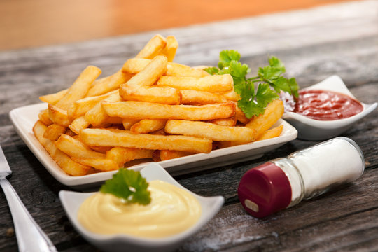 Bowls with french fries and parsley on the top with bowls with tomato sauce and mayonnaise