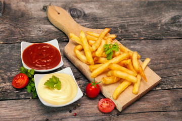 French fries on chopping board with tomato sauce and mayonnaise in bowls and cherry tomato