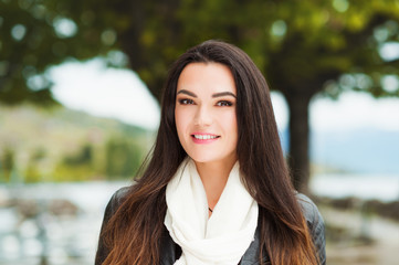 Fototapeta premium Outdoor portrait of beautiful brunette woman with long hair, wearing big white cashmere scarf and black leather jacket