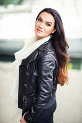 Outdoor portrait of beautiful brunette woman with long hair, wearing big white cashmere scarf and black leather jacket