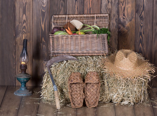Basket with vegetables, bast shoes, hay, straw hat in an old barn