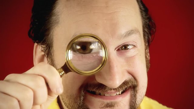 A funny ugly man looking at the camera with a magnifying lens (a detective / private eye), searching for valued information.
