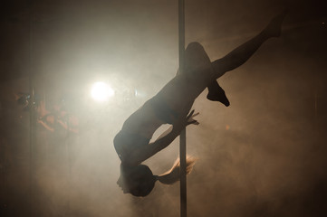 Young sexy woman exercise pole dance on a dark background