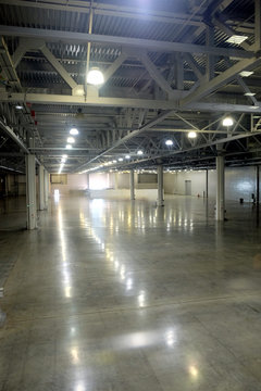 Large empty warehouse interior in an industrial building with high vertical columns with and high ceiling and artificial lighting