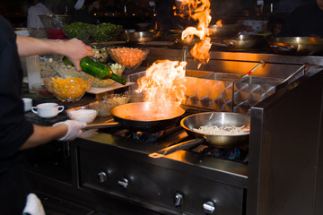 Chef in restaurant kitchen at stove with pan, doing flambe on food. low ligth selective focus.