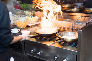 Chef in restaurant kitchen at stove with pan, doing flambe on food. low ligth selective focus.