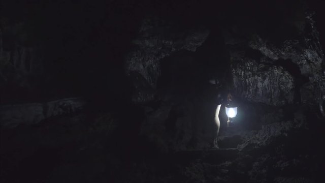 Girl walking through dark cave with lantern